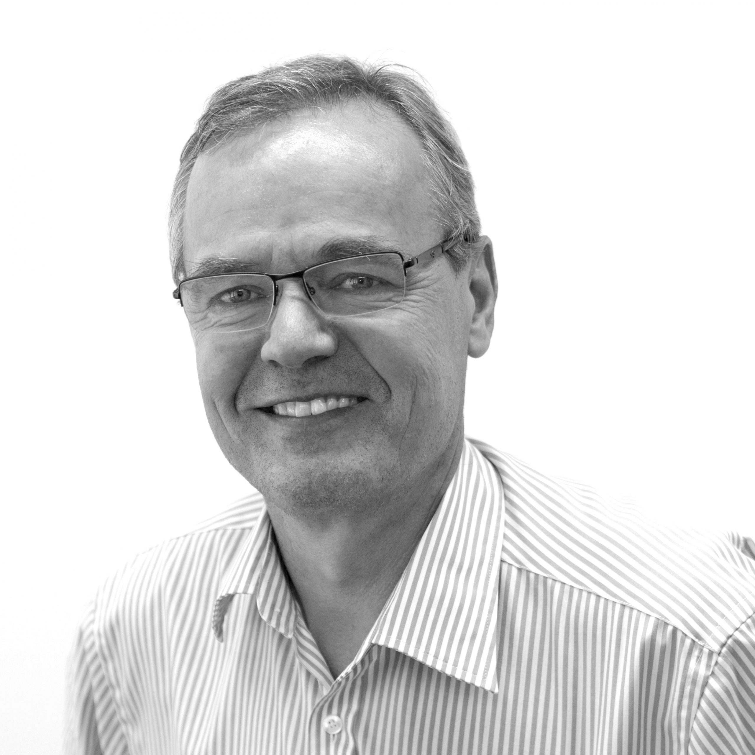 Black and white potrait of Tapio Toivanen smiling, white background.
