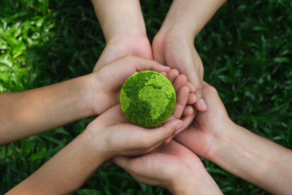 Three pair of hands holding a green globe